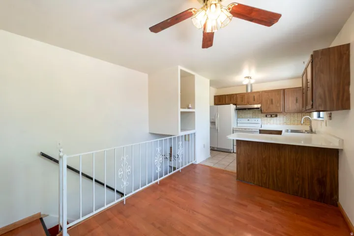 Wood-finish flooring with a white railing staircase, kitchen with wood cabinetry, and a ceiling fan