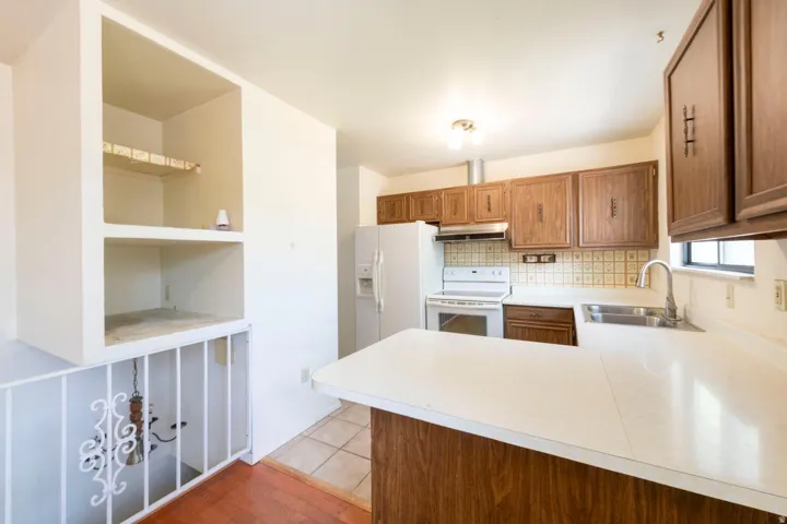 Kitchen with wood-finish cabinetry, solid surface countertops, a stainless steel sink, and white appliances
