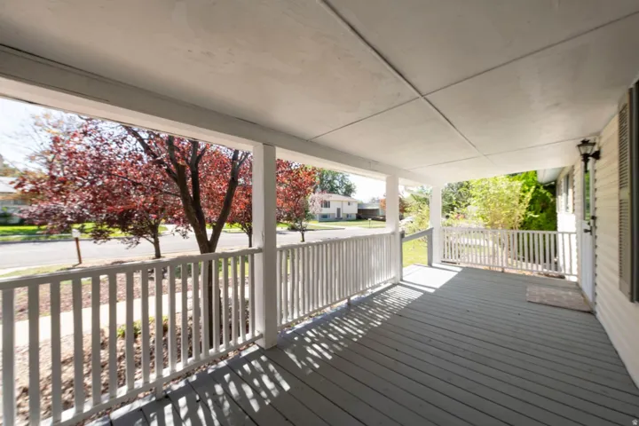 Covered porch with painted wood decking, white railings, and an exterior wall light fixture
