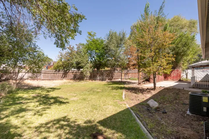 Expansive backyard featuring a manicured lawn, established trees, wood fencing, and a concrete patio