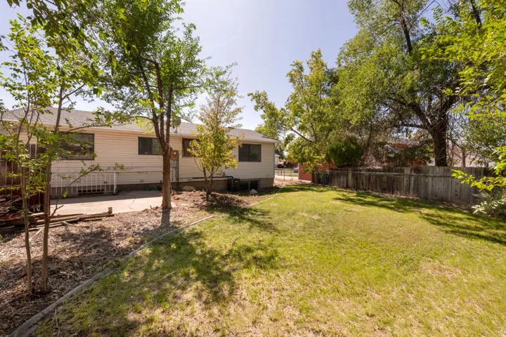 Expansive backyard featuring a lush lawn, mature trees, concrete patio, and a wood fence