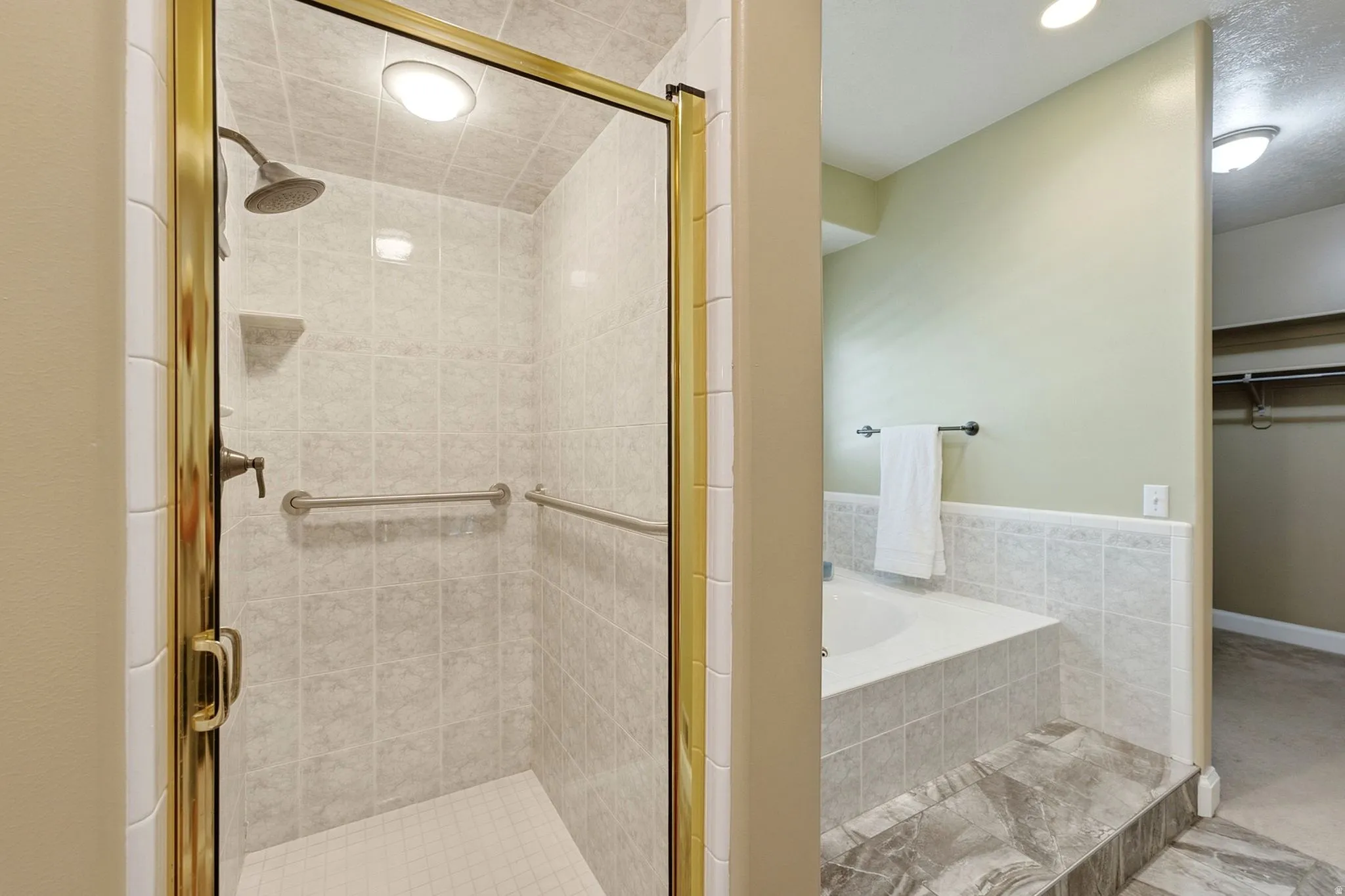 Tiled shower with brass-finish frame and fixtures, built-in corner shelf, and grab bars