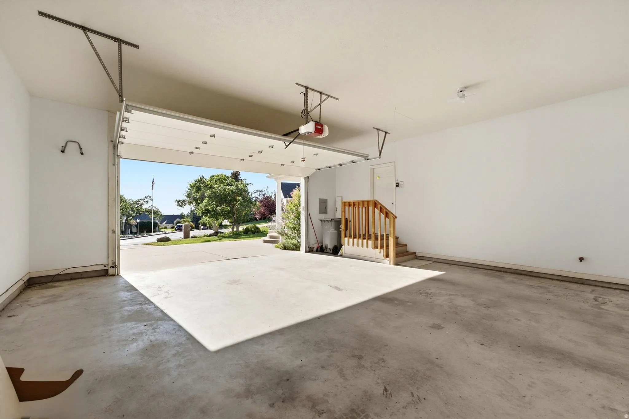 Garage with an automatic opener, interior staircase with wood railing, and concrete flooring