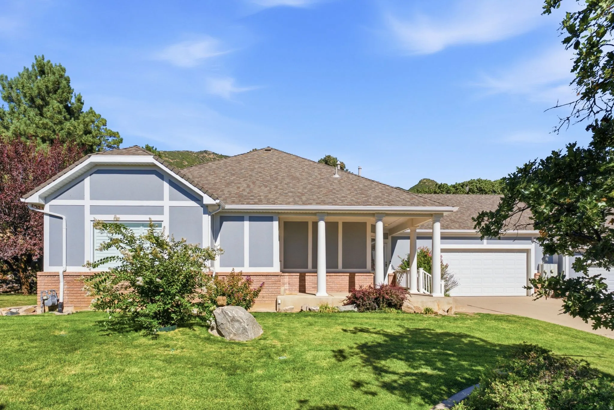 Single-story residence featuring a covered front porch with white columns, light blue siding with white trim, a brown shingle roof, and an attached two-car garage