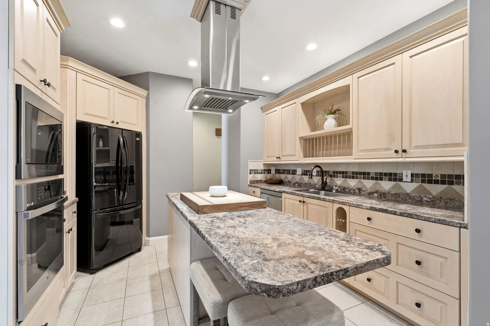 Light-toned cabinetry, stainless steel appliances, a kitchen island with seating, a built-in oven, and a mosaic tile backsplash