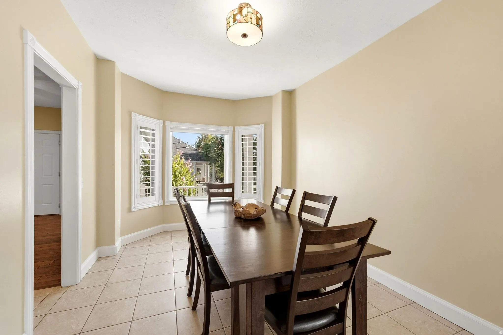 Bay window with white plantation shutters, tile flooring, and a semi-flush mount ceiling light fixture