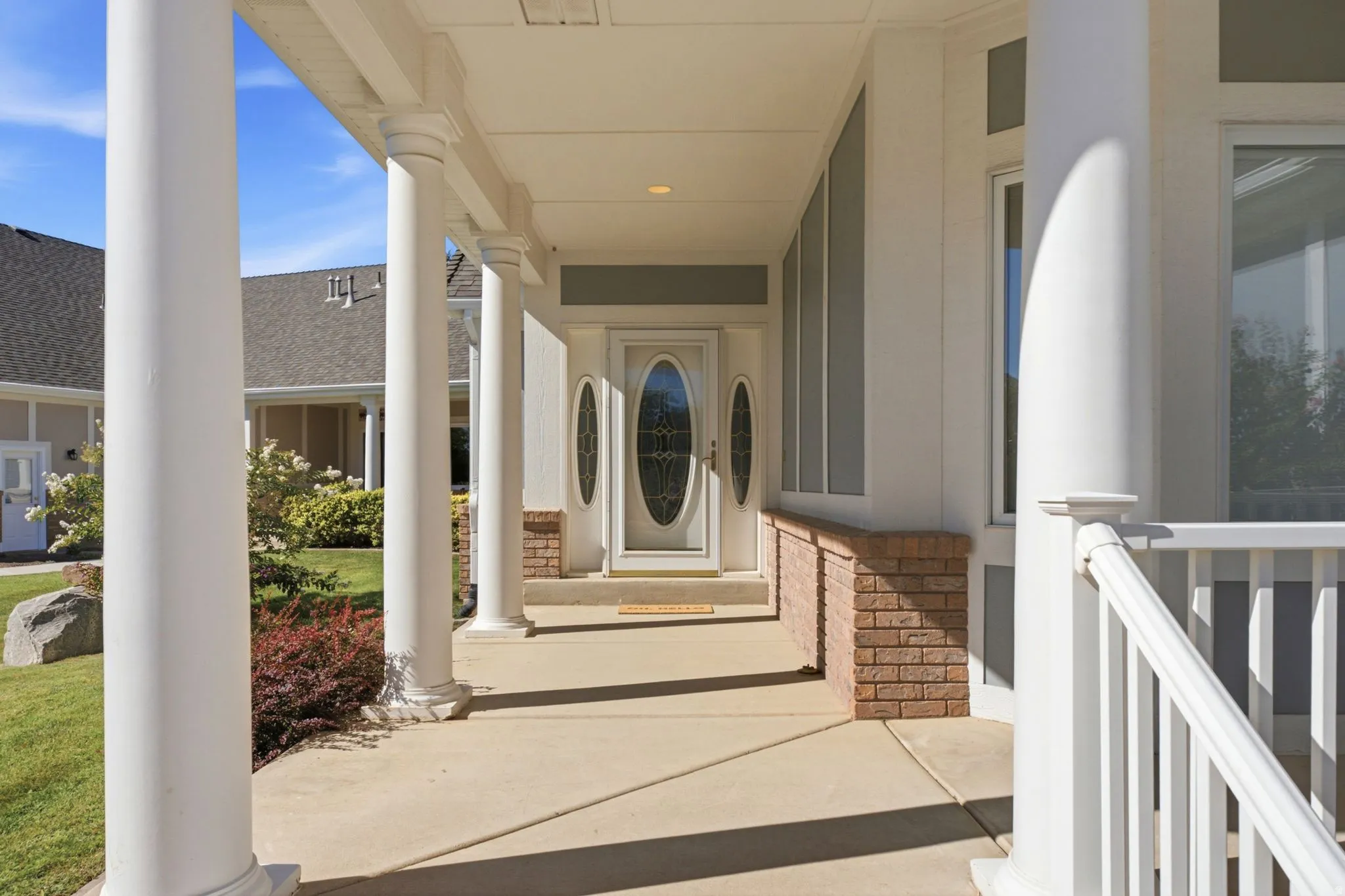 Covered front porch with classic columns, decorative oval glass entry door, and brick-clad foundation