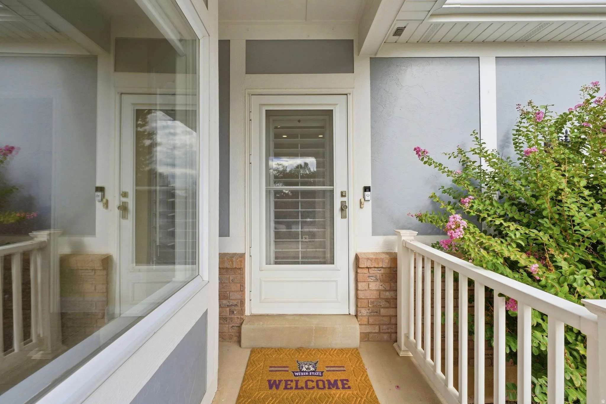 Front entry featuring a white paneled door with glass insert, brick pillar accents, and a white railing