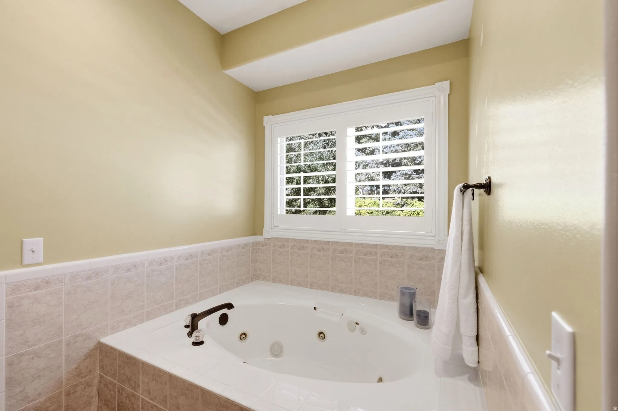 Built-in jetted tub with tiled surround, plantation shutters, and bronze fixtures