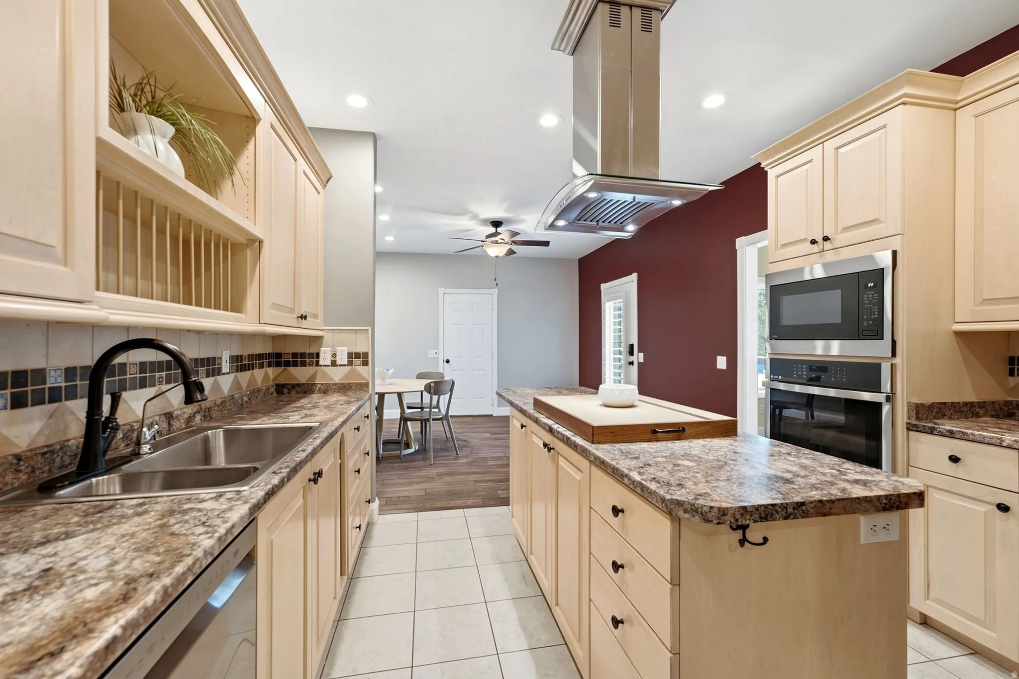 Kitchen featuring light wood-finish cabinetry, stainless steel appliances, a center island with countertop, and a tile backsplash