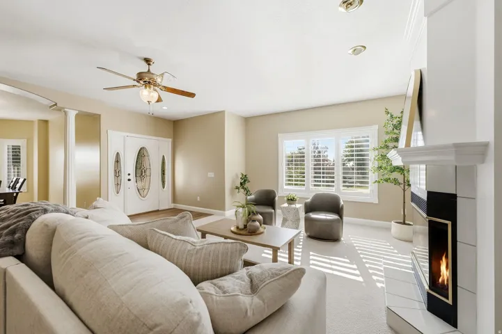 Recessed lighting, ceiling fan, white double entry doors with decorative glass, multiple windows with plantation shutters, and a fireplace with a white mantel