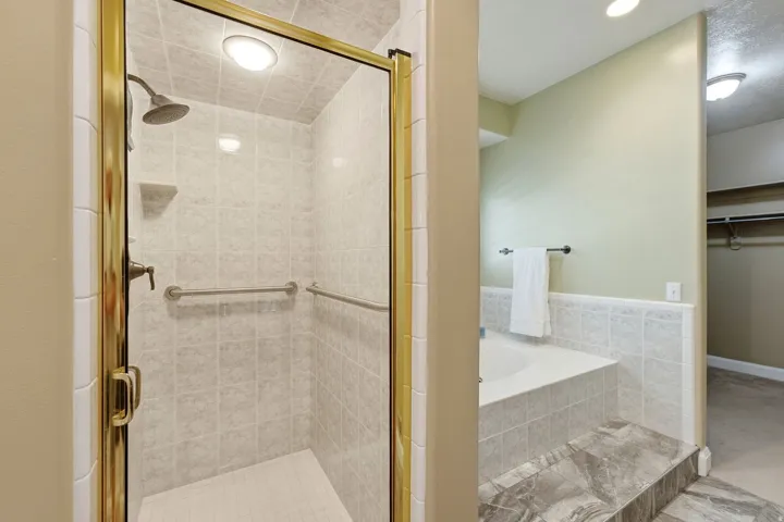Tiled shower with brass-finish frame and fixtures, built-in corner shelf, and grab bars