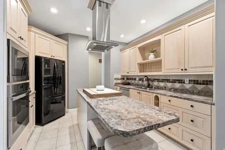 Light-toned cabinetry, stainless steel appliances, a kitchen island with seating, a built-in oven, and a mosaic tile backsplash