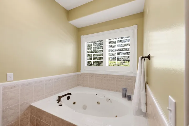 Built-in jetted tub with tiled surround, plantation shutters, and bronze fixtures