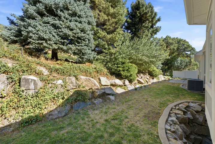 Tiered landscaping with natural rock retaining walls, mature trees, manicured lawn area, and a rock-lined garden bed