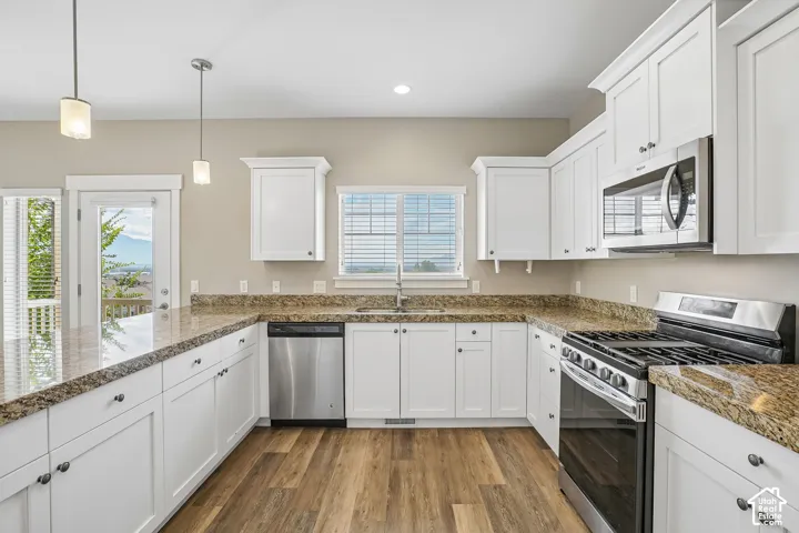 Kitchen featuring white cabinetry, wood-finish flooring, stainless steel appliances, pendant lighting, and stone countertops