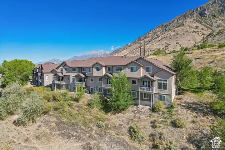 Multi-story property with balconies, a pitched roof, and visible mountain scenery