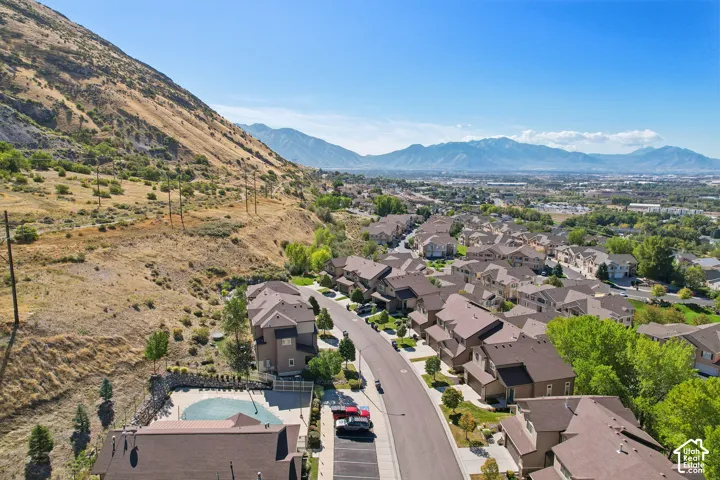 Community featuring a residential street, multiple properties with brown-shingled roofs, a swimming pool, and mountainous terrain
