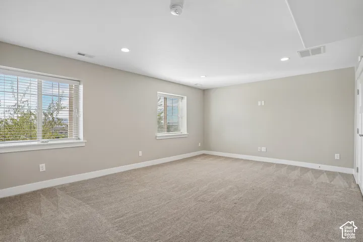Recessed lighting, light-colored carpeting, two windows with blinds, and neutral wall tones