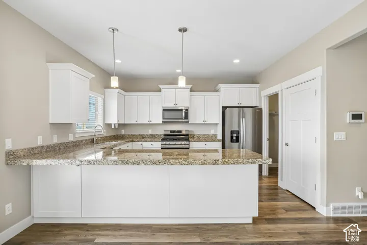 White cabinetry, stainless steel appliances, wood-finish flooring, recessed lighting, and a kitchen island with pendant lighting