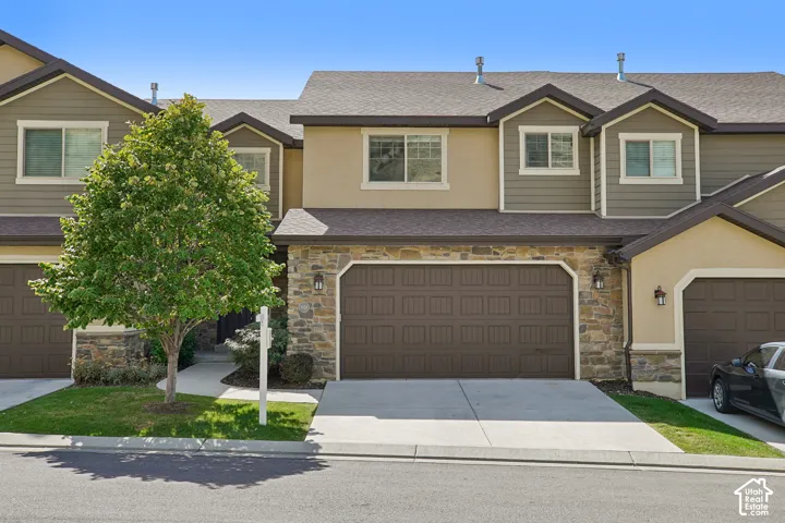 Stone veneer accents, two-car garage, dormer windows, and a manicured front lawn