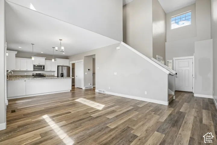 Open-concept living area featuring wood-finish flooring, a kitchen with white cabinetry and stainless steel appliances, a multi-level ceiling, and a prominent staircase