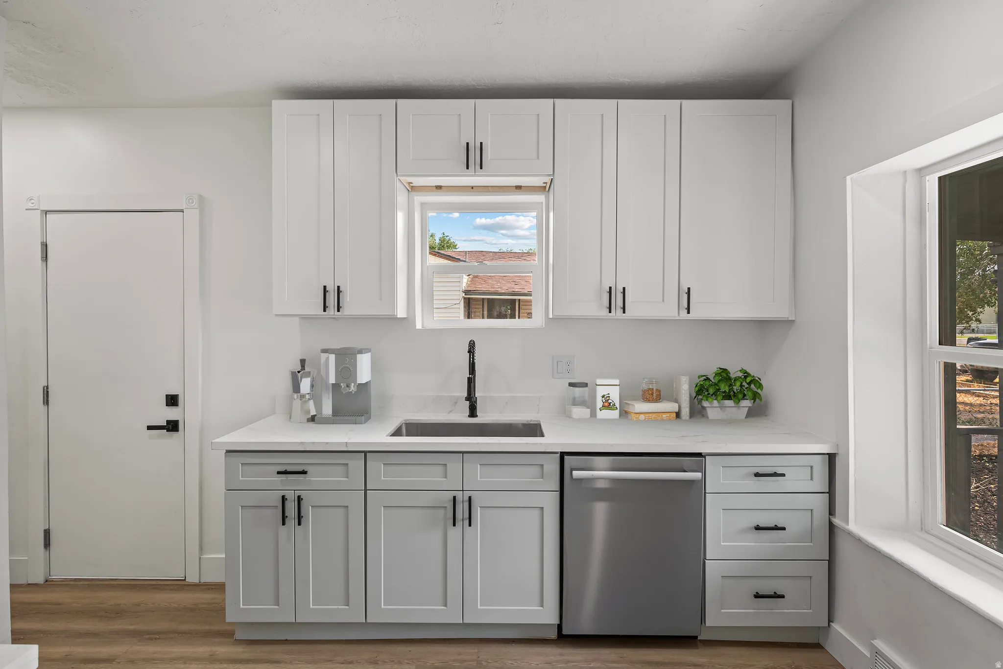 Two-tone cabinetry with matte black hardware, stainless steel dishwasher, undermount sink with a black faucet, and wood-finish flooring