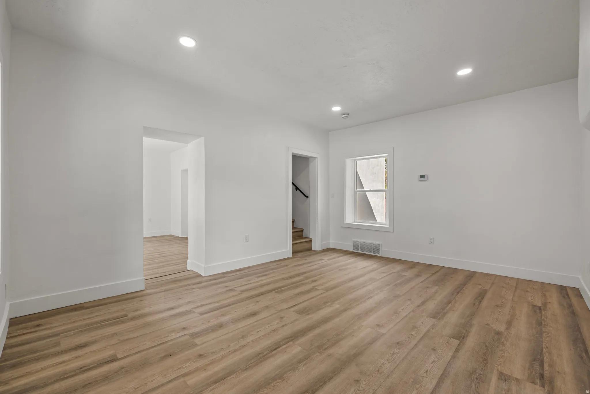 Recessed lighting, wood-finish flooring, white walls, white trim, and a window with white casing