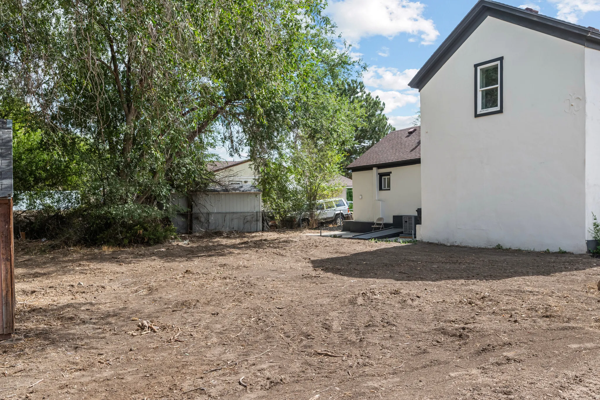 Expansive side yard with a substantial mature tree and a white stucco exterior featuring dark trim