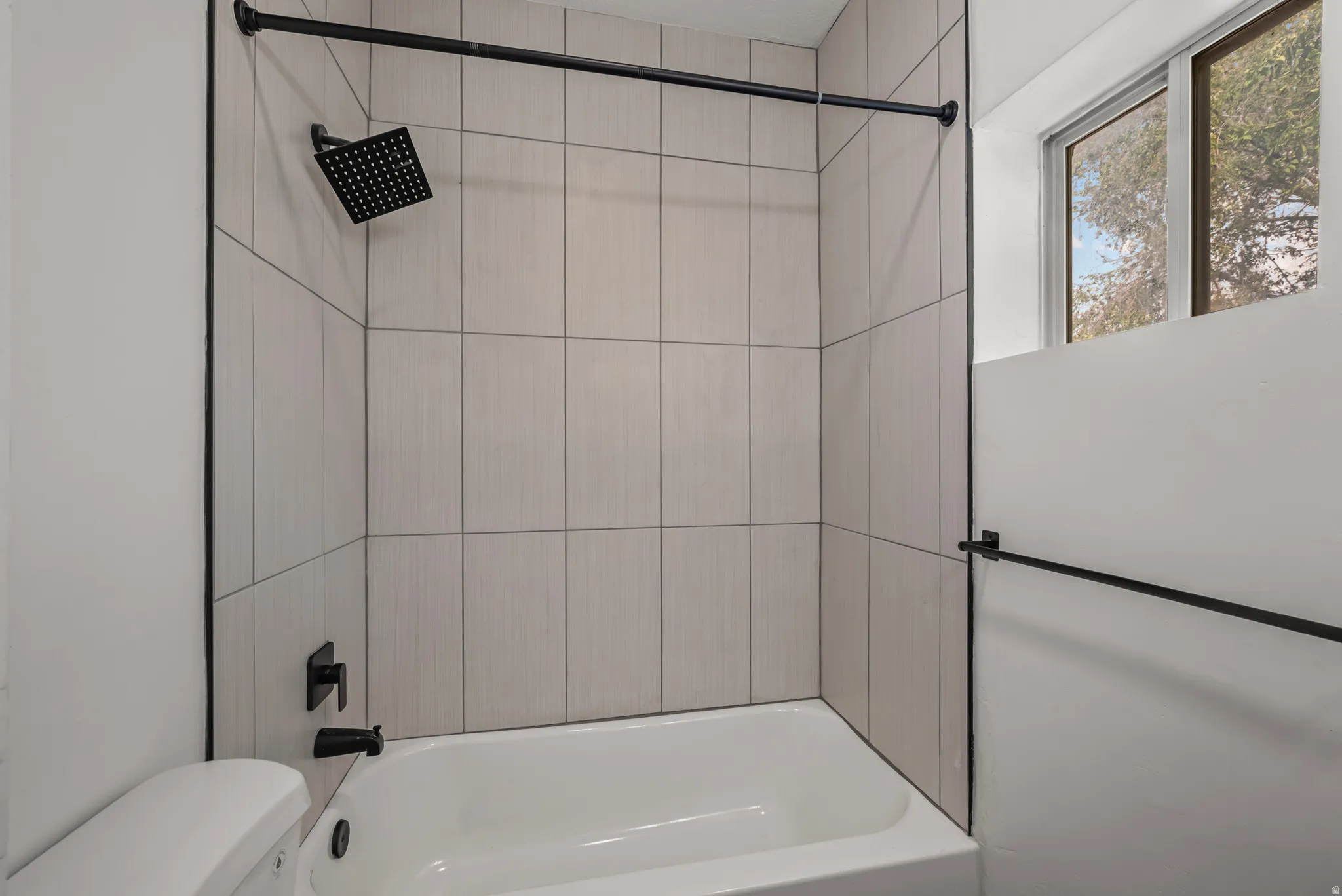 Bathtub with light-toned tiled surround, matte black rainfall showerhead, and coordinating matte black fixtures