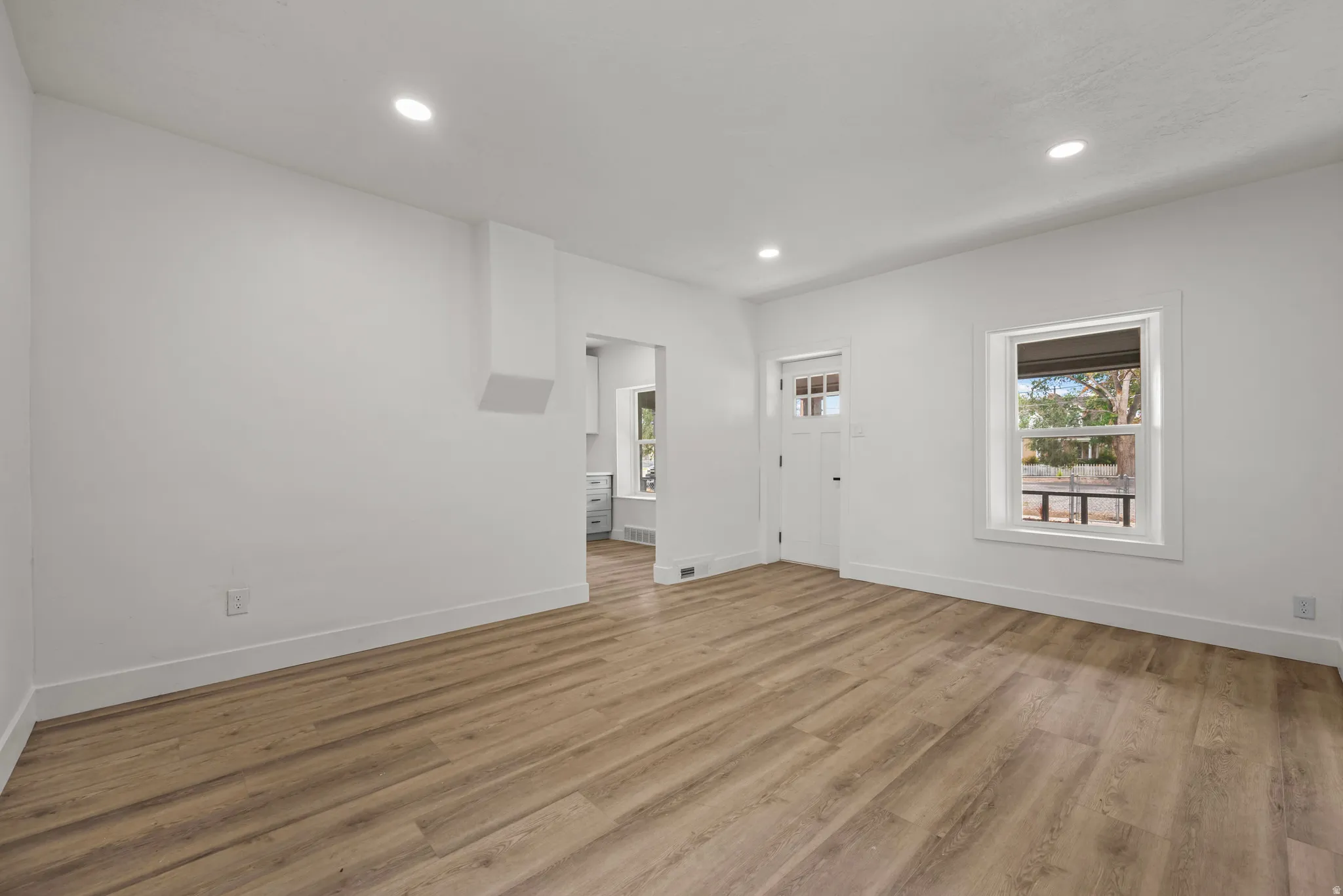 Recessed lighting, wood-finish flooring, white trim, and a window with white casing