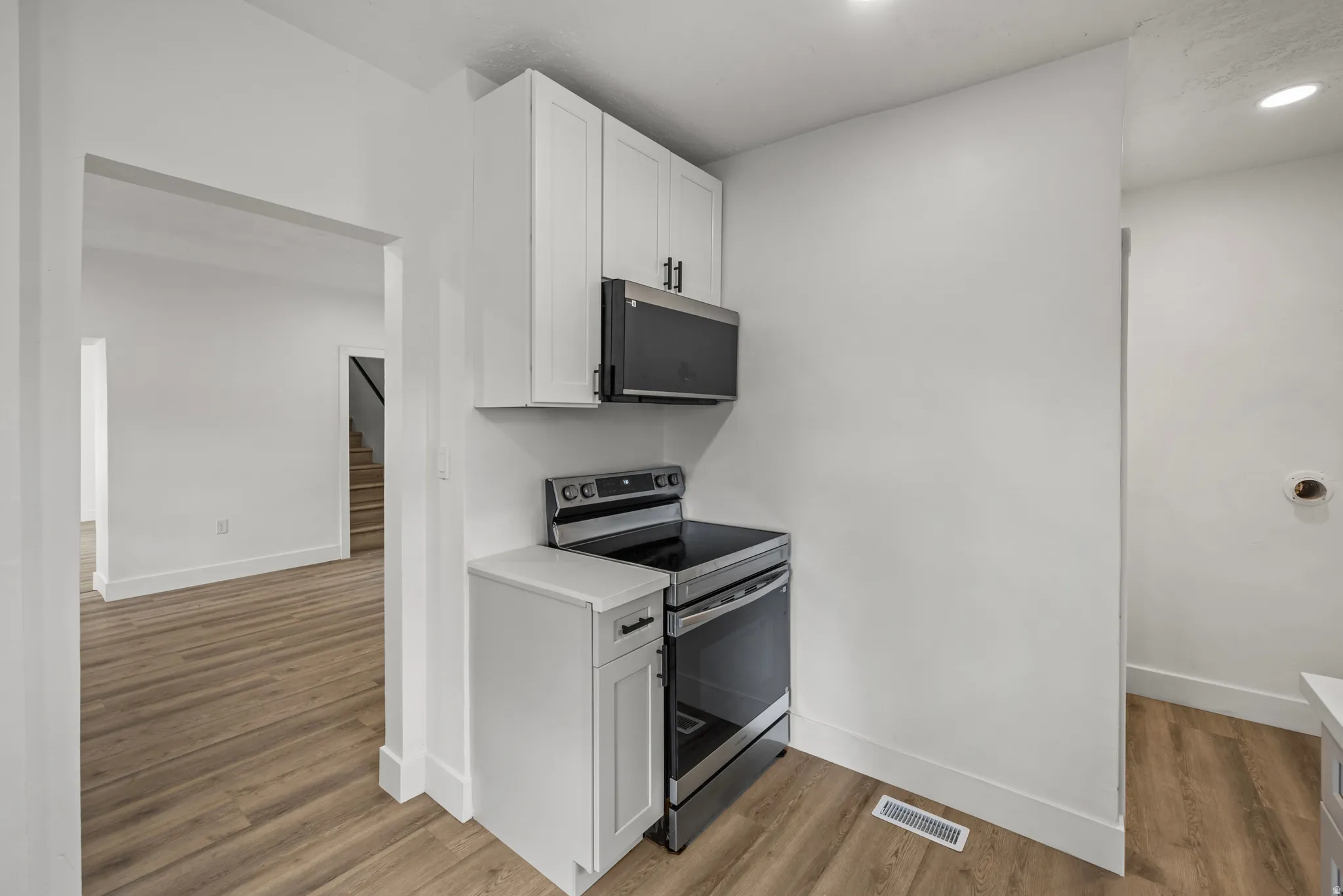 White shaker cabinetry, stainless steel range and microwave, light wood-finish flooring, and recessed lighting