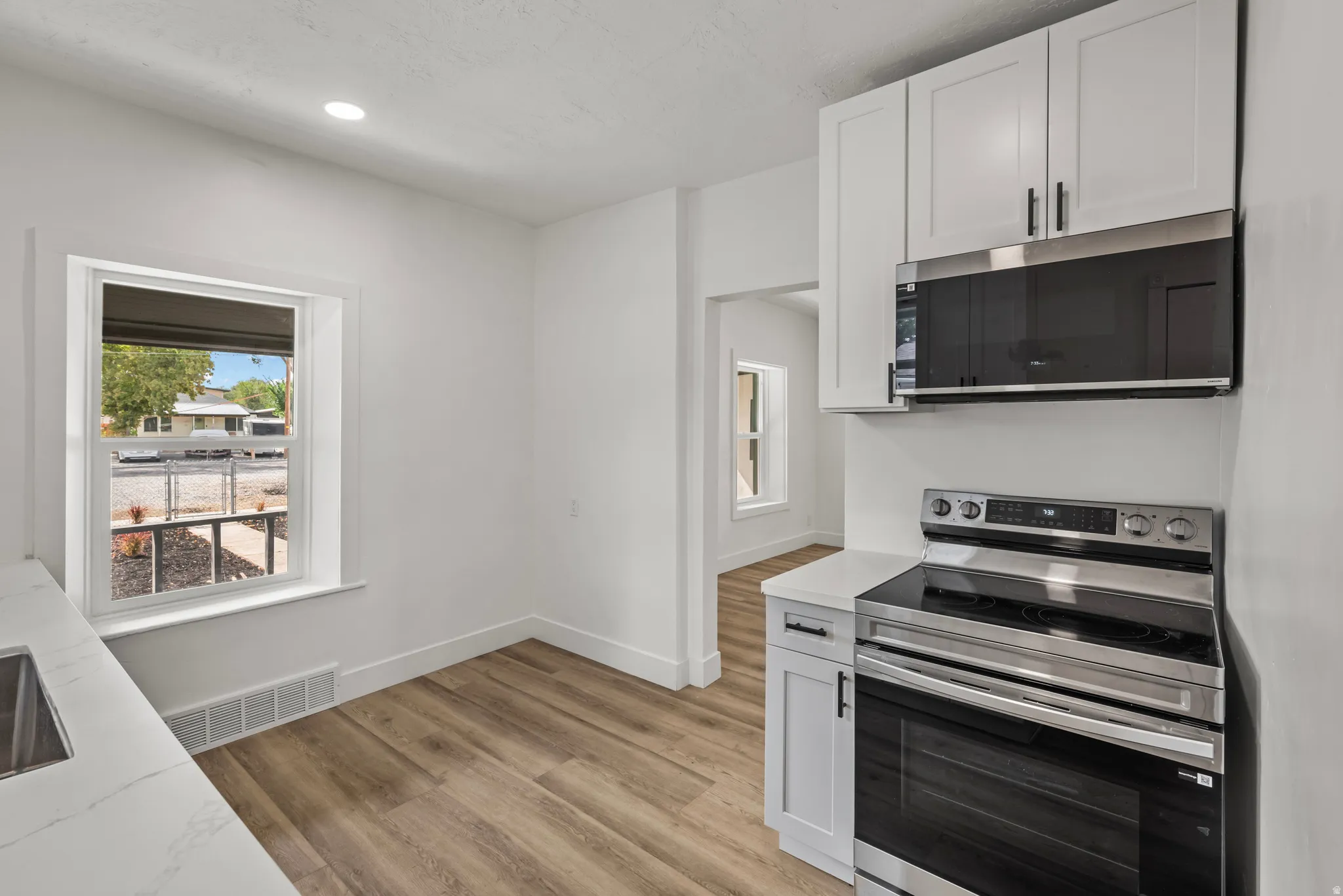 White shaker cabinetry with matte black hardware, stainless steel appliances, wood-finish flooring, recessed lighting, and white quartz countertops