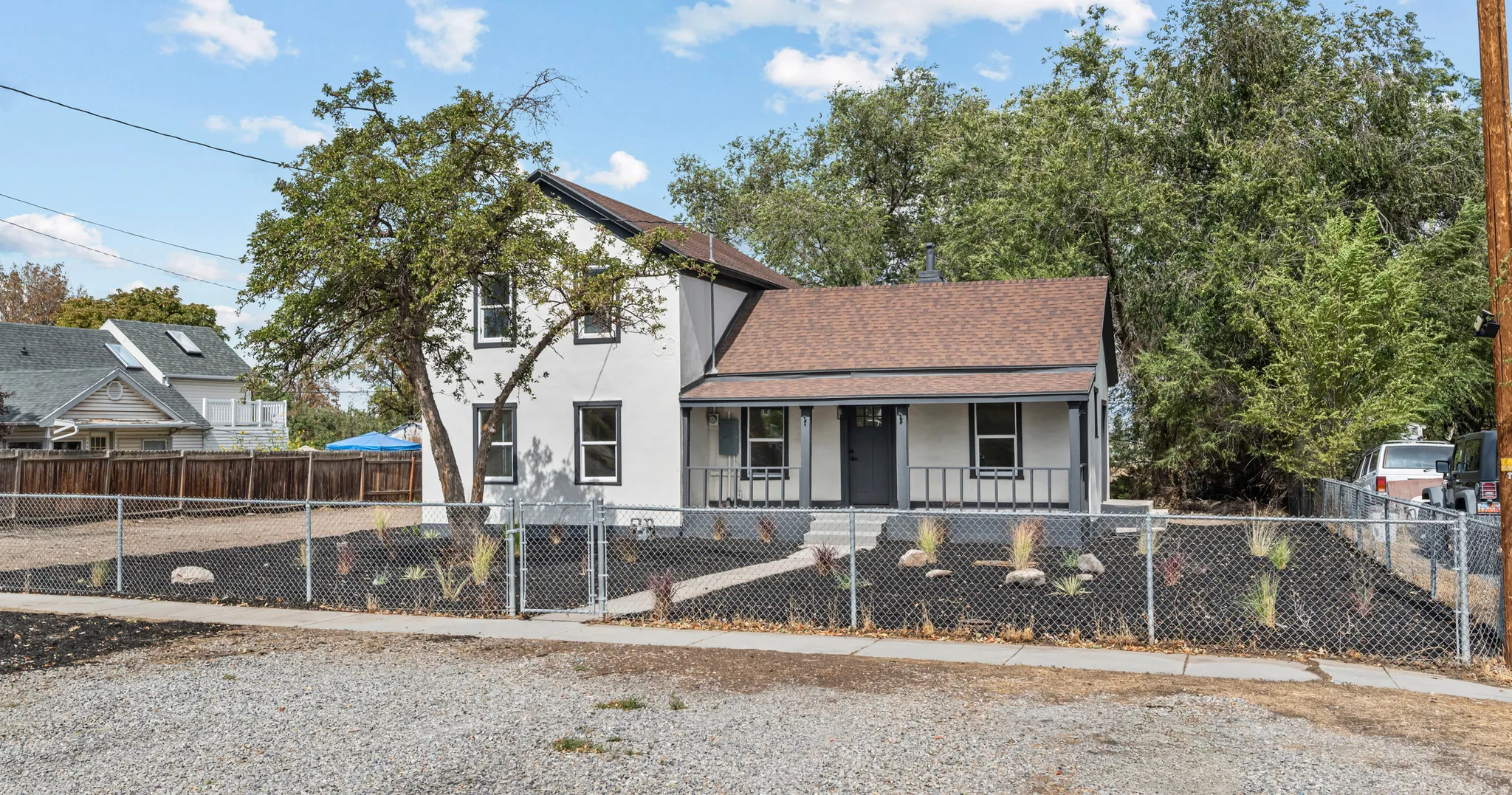 Two-story exterior with white siding and dark trim, covered front porch, gravel front yard, and chain-link fencing