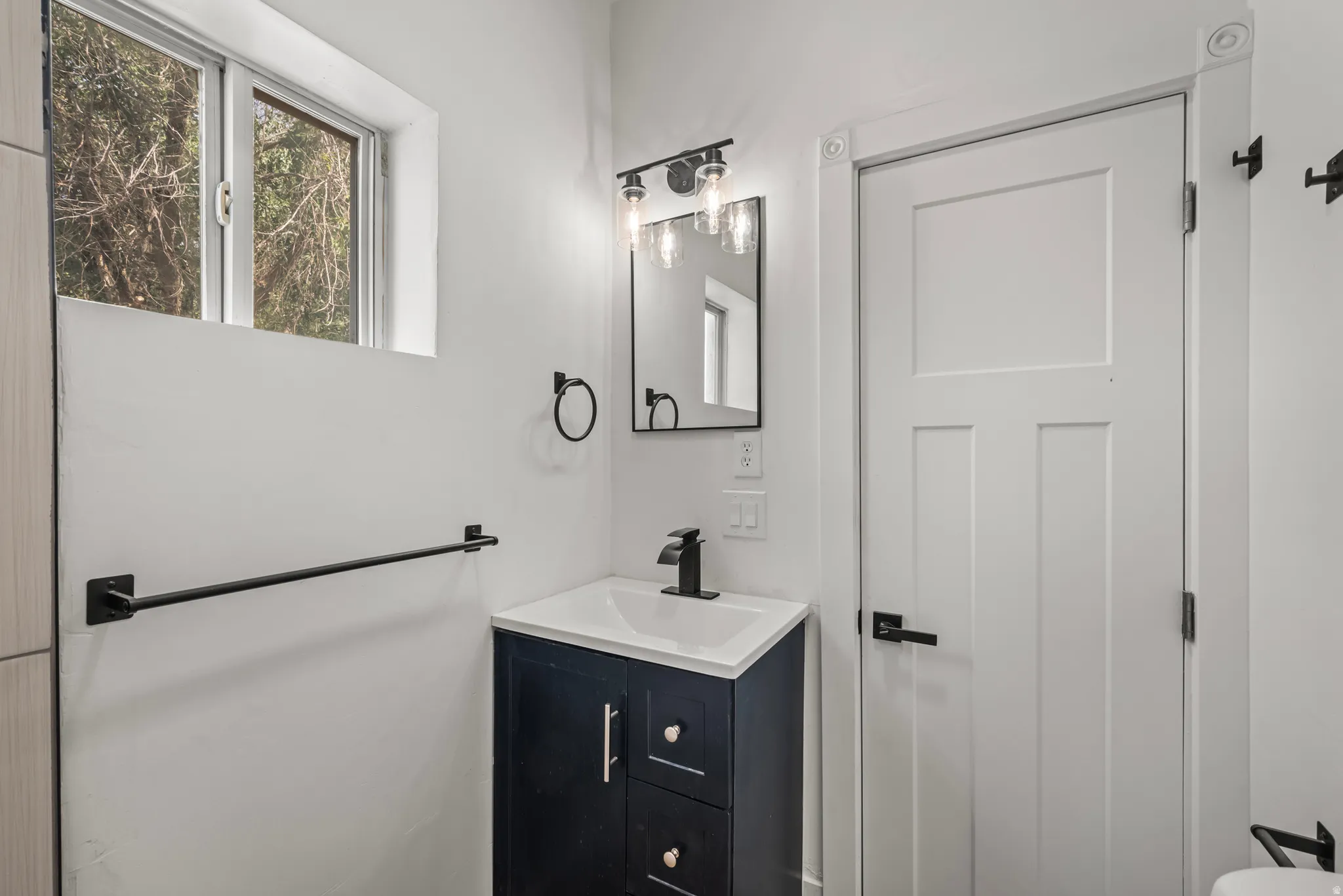 Window with natural light, dark blue vanity with white countertop, black fixtures, and white paneled door