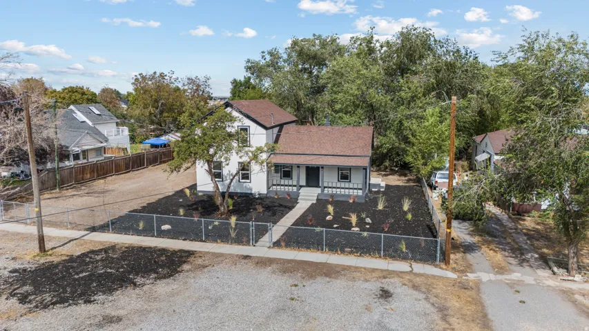 Two-story exterior with white siding and dark trim, featuring a covered porch, a newly landscaped front yard with black mulch and young plantings, and a chain-link fence