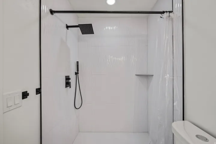 Walk-in shower featuring textured white tile, a matte black rainfall showerhead, and a built-in corner shelf
