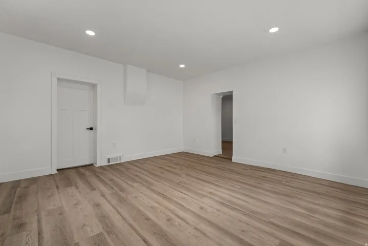 Recessed lighting, wood-finish flooring, white walls, and a white paneled door with black hardware