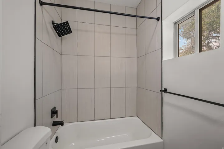 Bathtub with light-toned tiled surround, matte black rainfall showerhead, and coordinating matte black fixtures