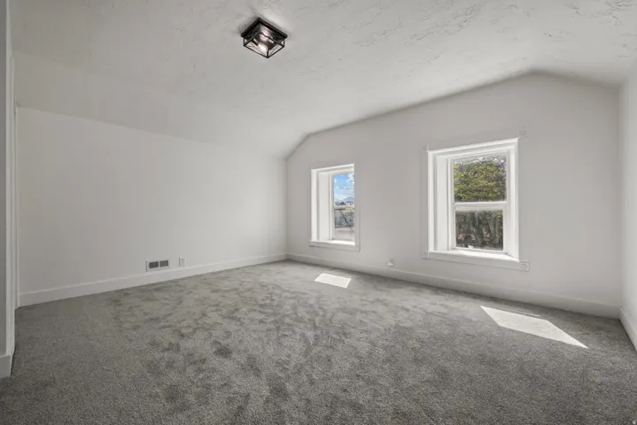 Light gray wall-to-wall carpeting, white painted walls, two double-hung windows, and a black flush-mount ceiling light fixture