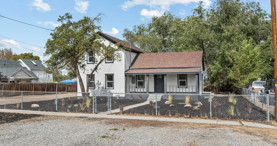 Two-story exterior with white siding and dark trim, covered front porch, gravel front yard, and chain-link fencing