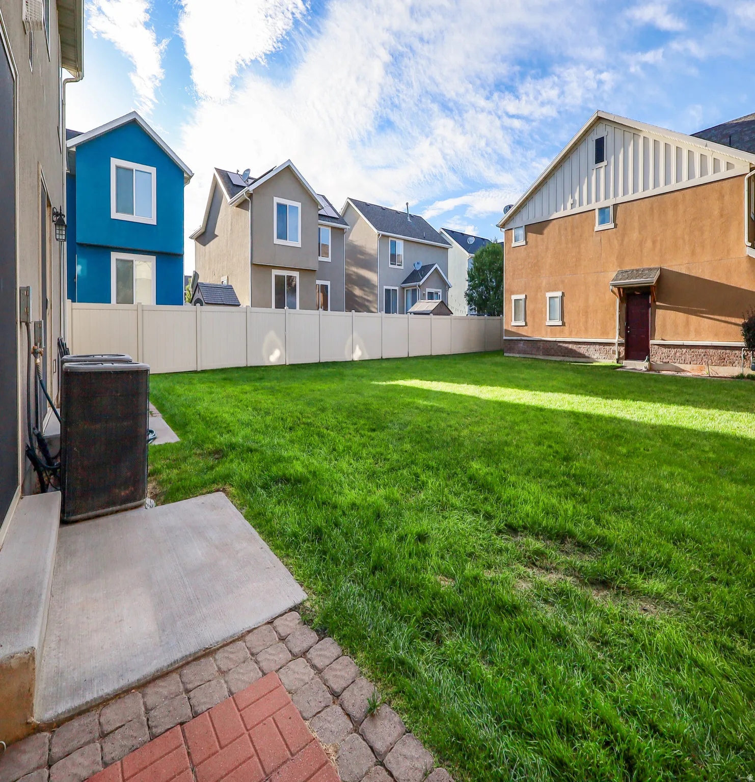 Expansive grassy yard with a concrete patio, brick paver accents, and privacy fencing