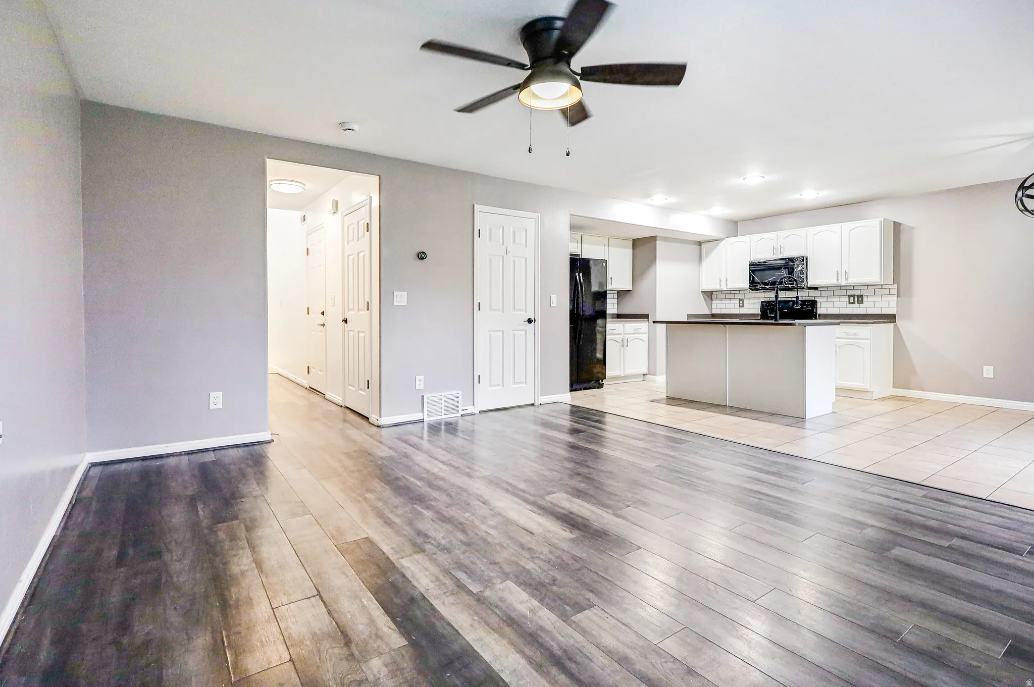 Wood-finish flooring, recessed lighting, ceiling fan, white cabinetry, and a kitchen island with countertop