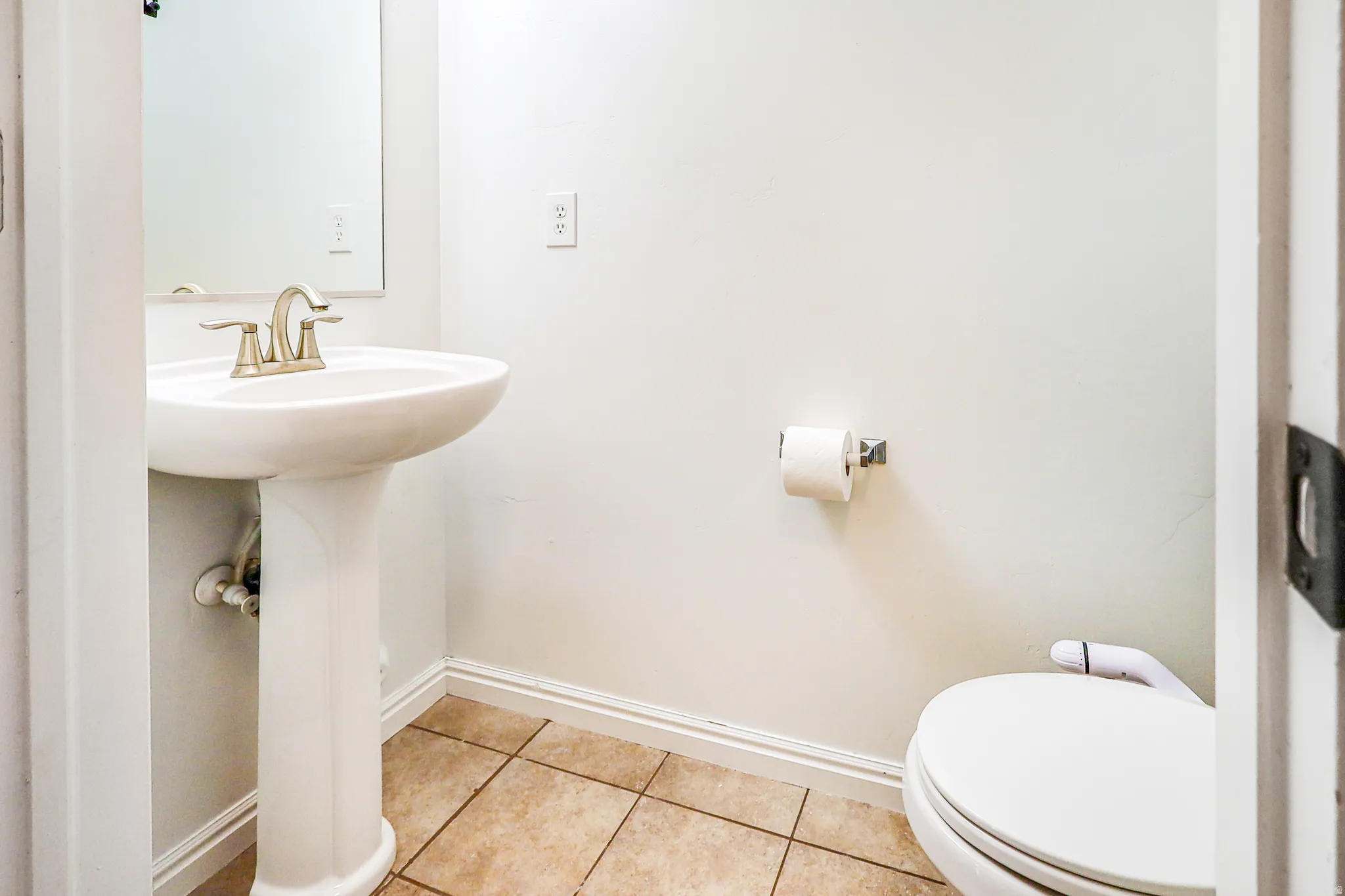 White pedestal sink with a brushed nickel faucet, framed mirror, and ceramic tile flooring