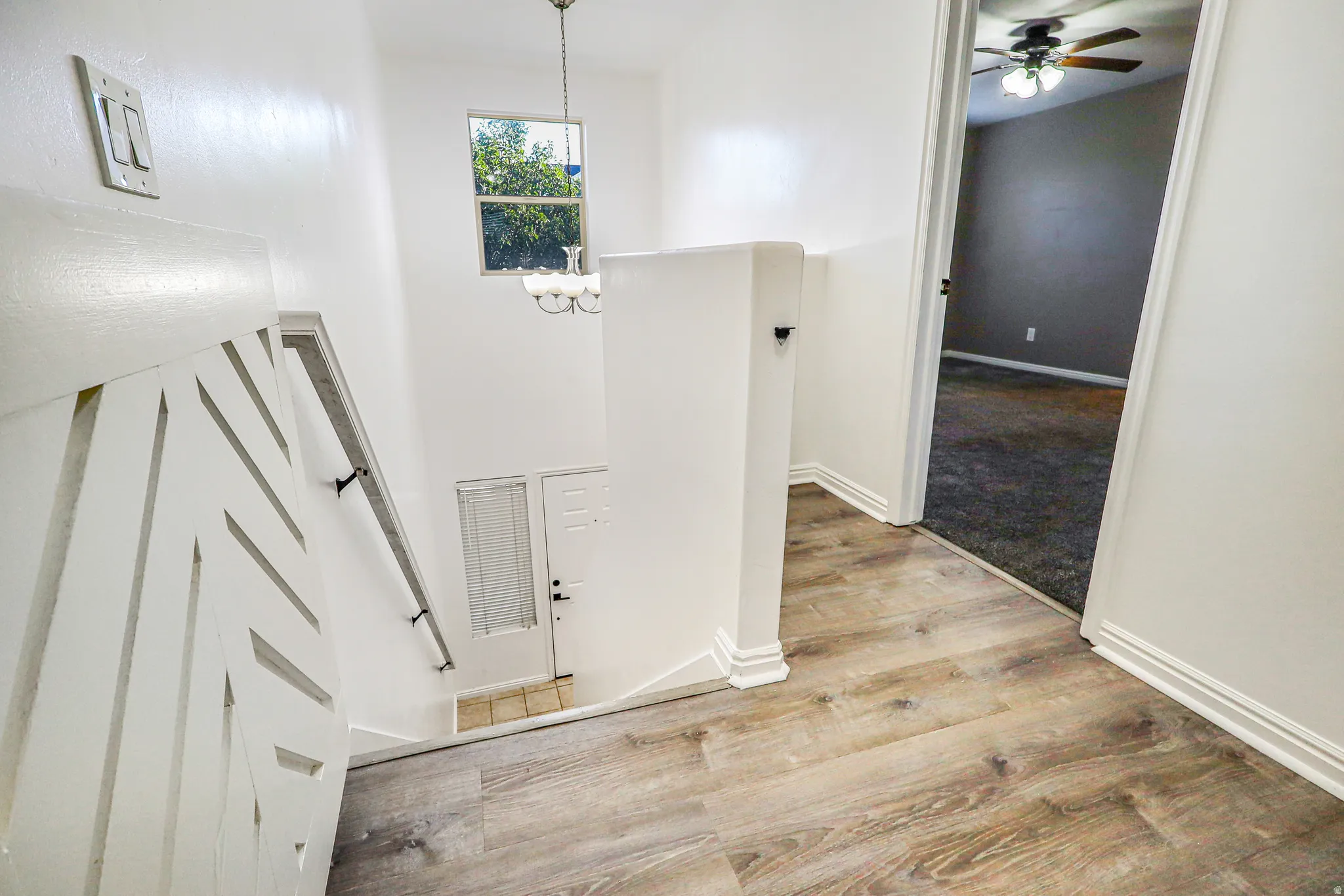 Wood-finish flooring, white walls, overhead lighting fixture, window, and a ceiling fan in the adjacent room