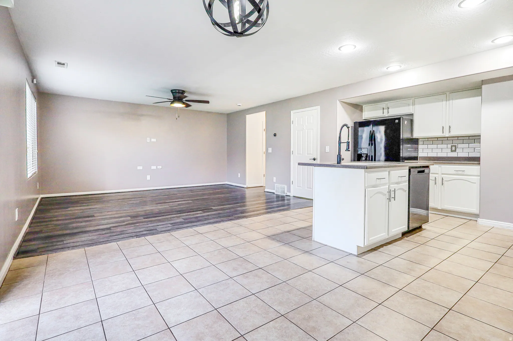 Open-concept kitchen and living area featuring a central island, white cabinetry, subway tile backsplash, and stainless steel appliances
