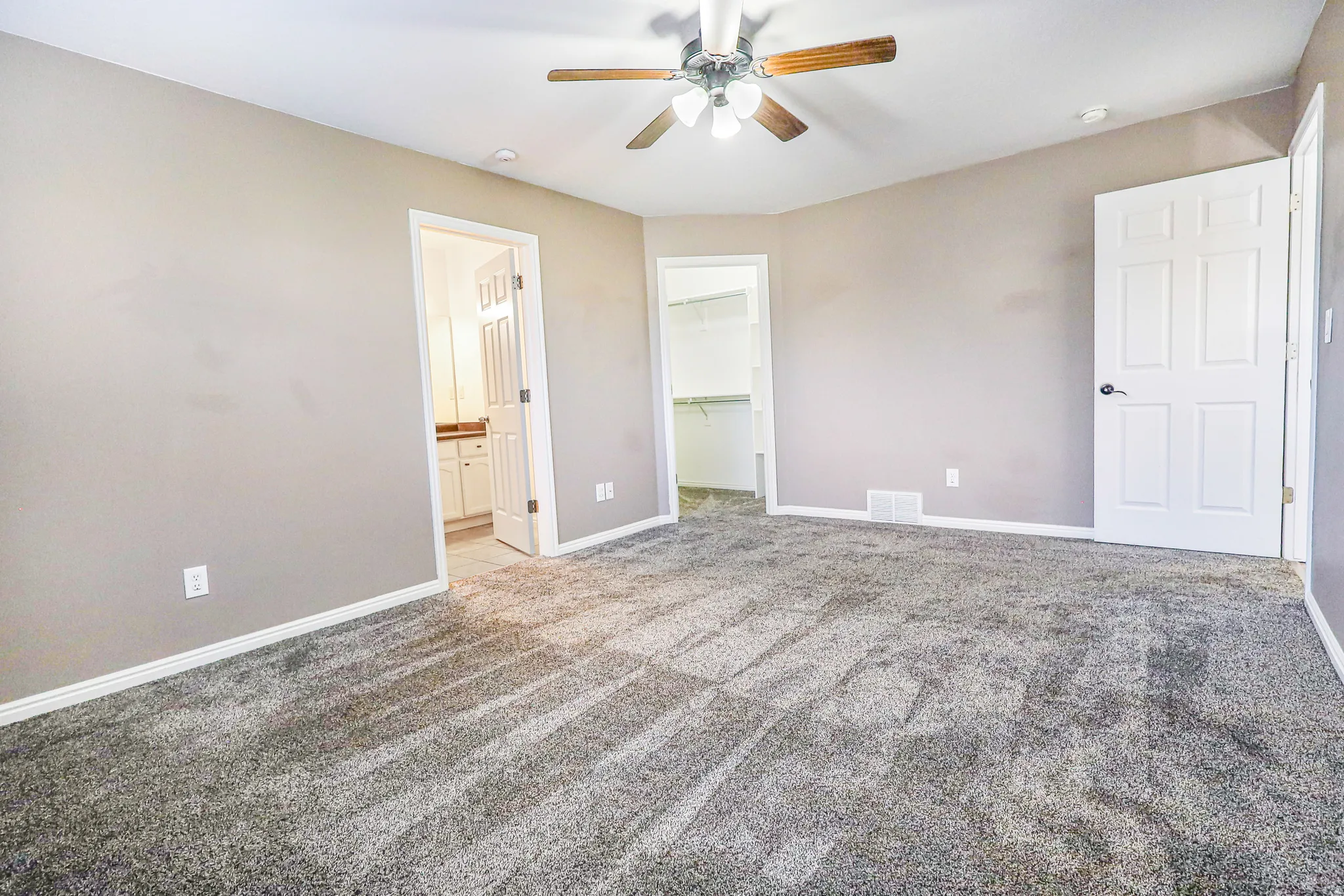 Plush carpeted flooring, neutral wall tones, ceiling fan with integrated lighting, two-panel interior doors, and a walk-in closet with built-in shelving