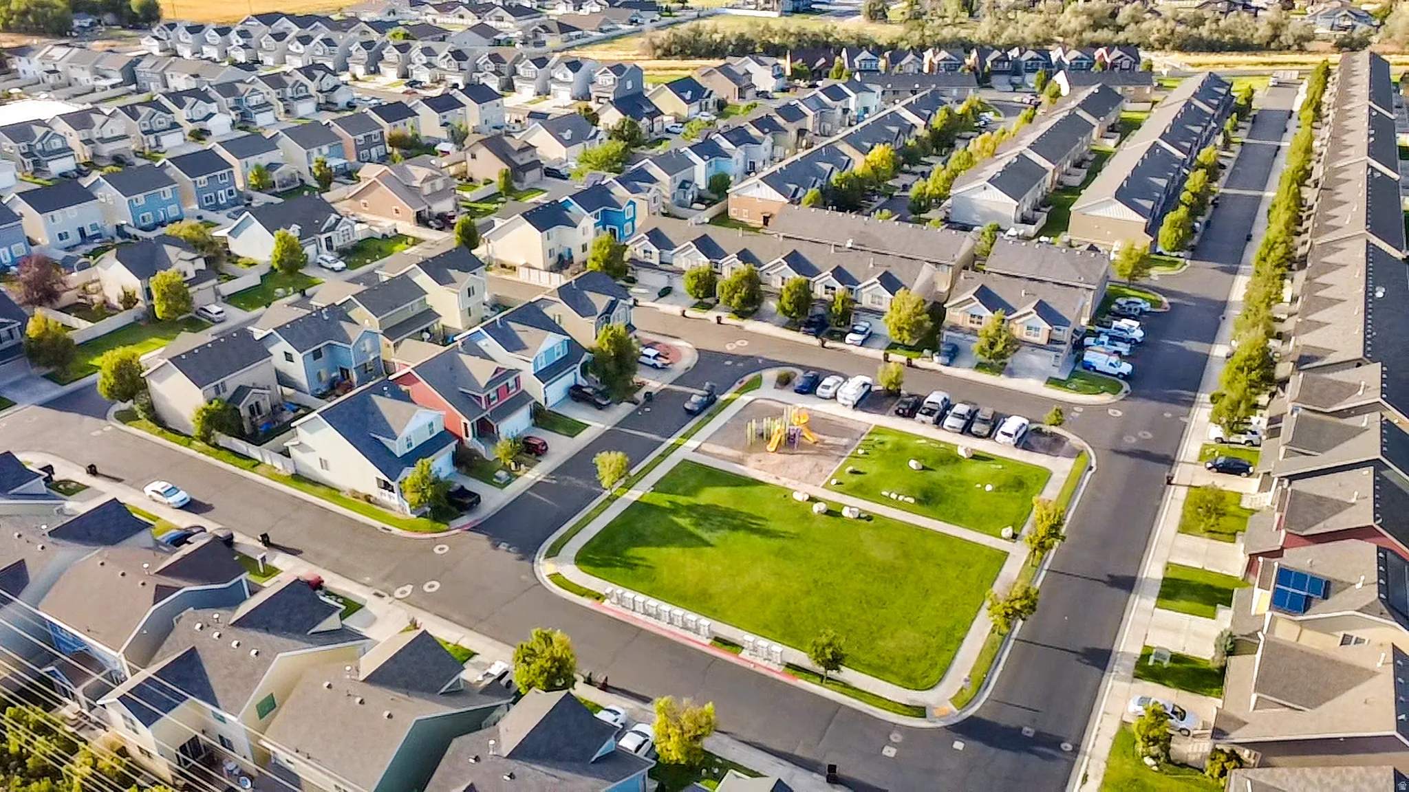 Residential development featuring a central green space with playground equipment, paved roadways, and mature landscaping