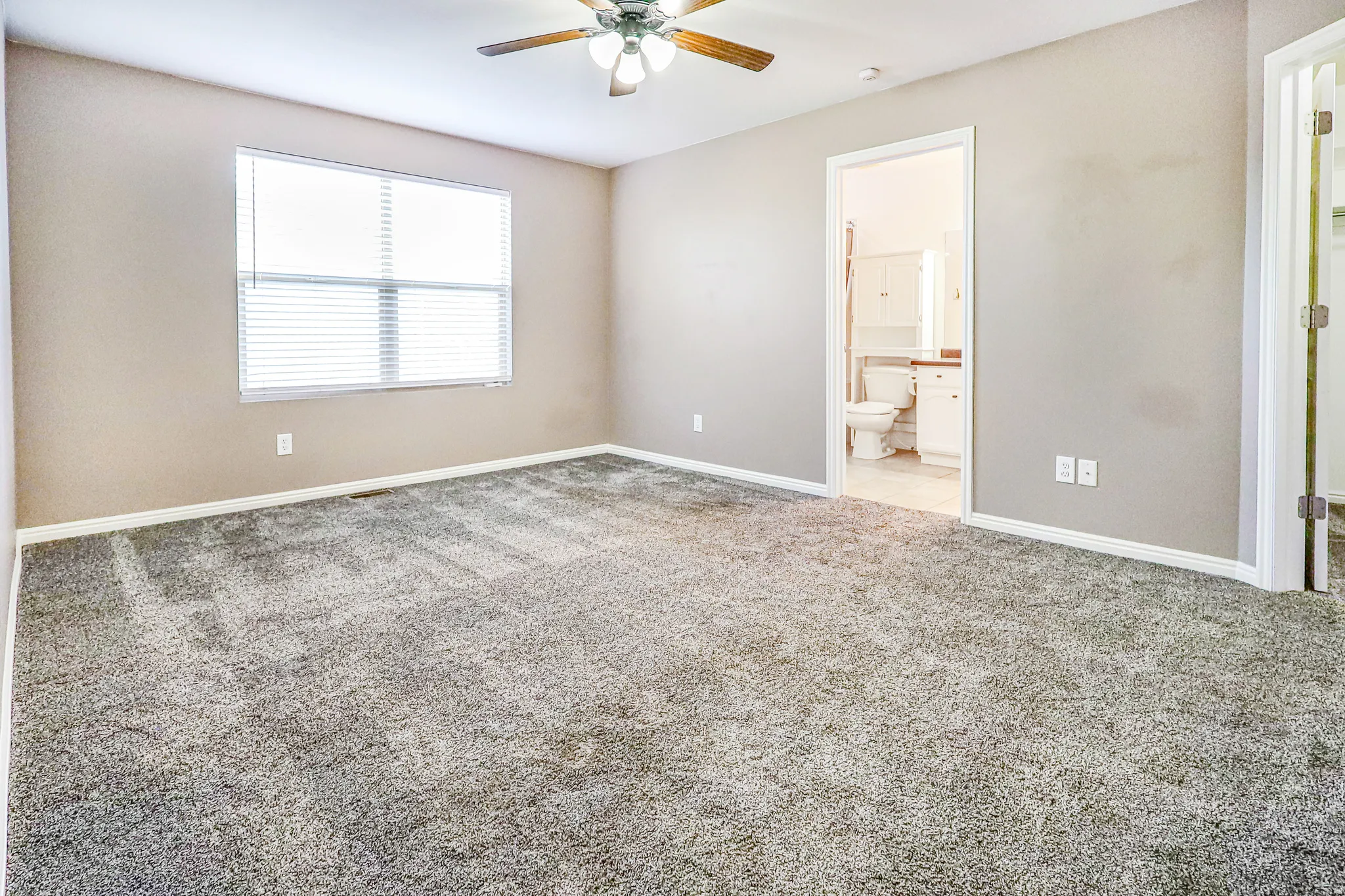 Carpeted interior with light-toned walls, ceiling fan, and window with blinds