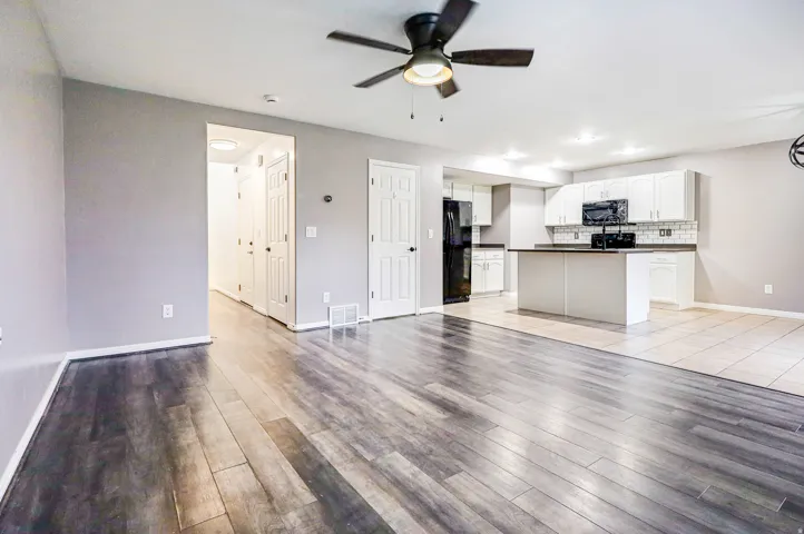 Wood-finish flooring, recessed lighting, ceiling fan, white cabinetry, and a kitchen island with countertop
